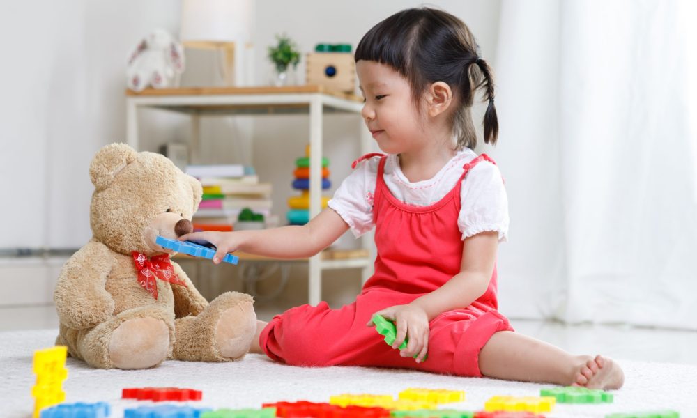 Preschooler girl learns at school. Cute child playing with teddy bear. Little girl having fun indoors at home, kindergarten or
day care. Educational concept for school kids.